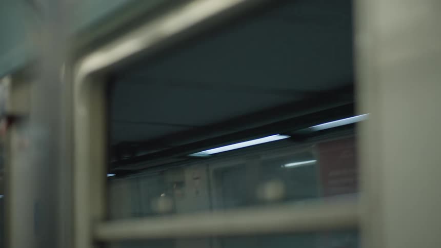 An abstract view from inside a moving subway train shows the reflection of the station passing by