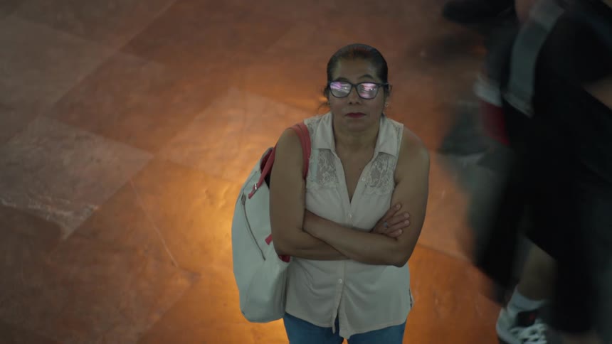 High angle view of a woman standing perfectly still as a time-lapse crowd rushes by in a blur of motion
