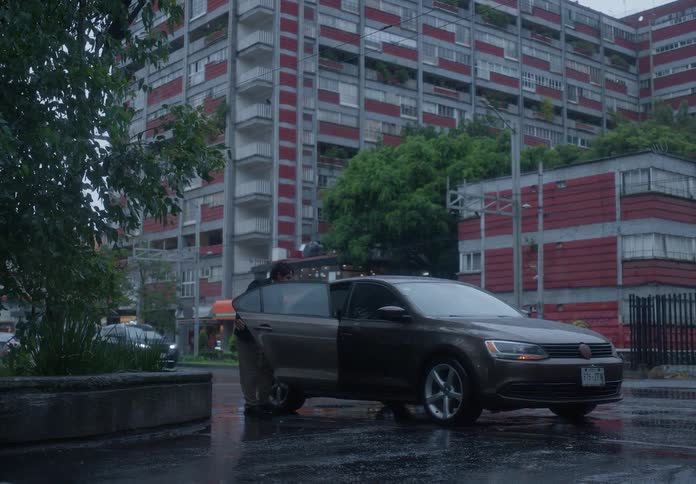 A man holding an umbrella hails a car on a rainy city street and gets into the back seat after it pulls over