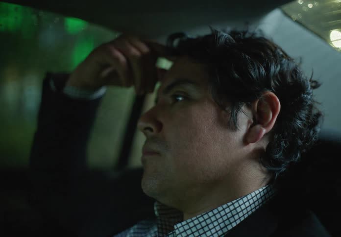 A close-up on a smartphone with a green screen transitions to a tired businessman resting in the back of a car on a rainy night