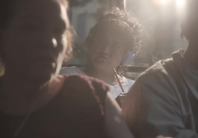 Dreamy slow-motion shot of a focused young woman with curly hair listening to music and studying on a bus as the sun flares through the window