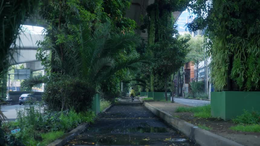 A person cycles through a lush green corridor of plants and trees growing beneath a city highway overpass