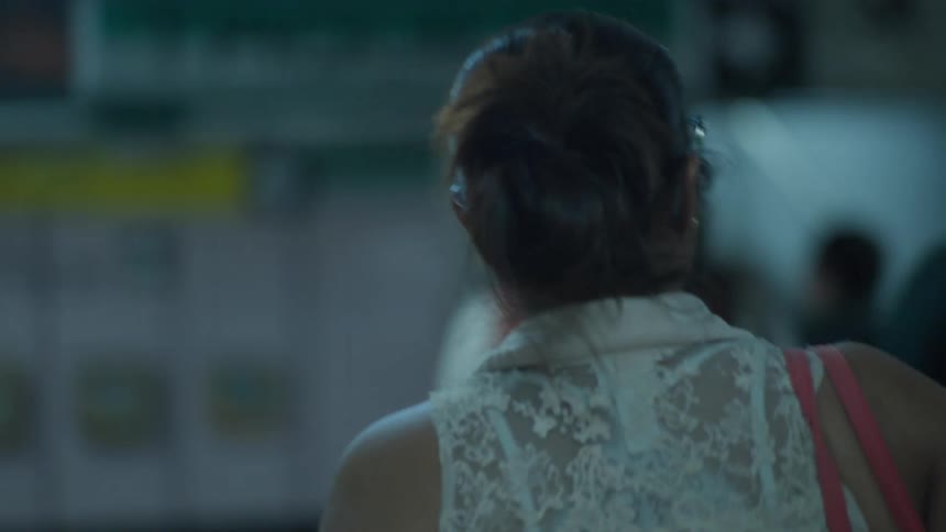 An over-the-shoulder slow-motion shot of a woman with her hair in a bun navigating a crowded, dimly lit underground station