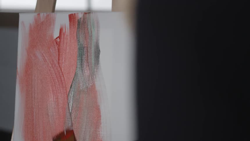 Red paint is smeared onto a canvas with a brush