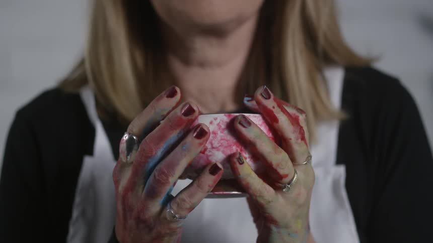 Woman with paint covered hands holds a paint covered mug