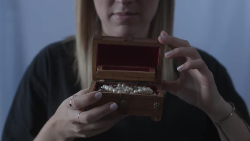 A woman closes a jewelry box containing pearls