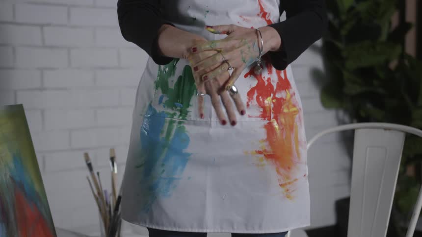 A woman wearing an apron rubs her paint stained hands