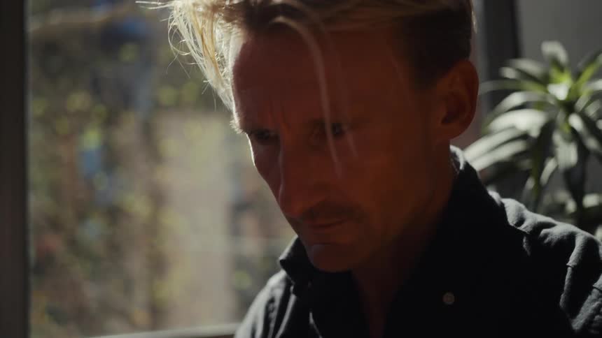 Close-up of a thoughtful man working from his sunny home office with a steaming mug on his desk