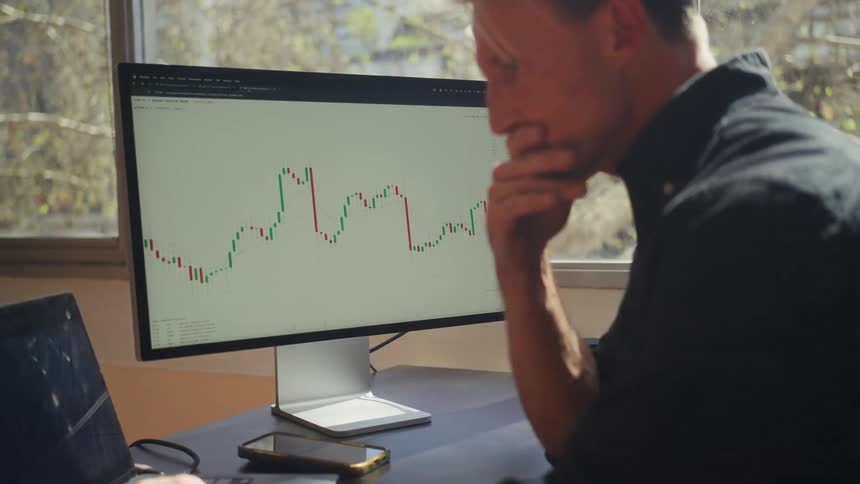 A focused day trader analyzes stock market candlestick charts on his computer and smartphone from his office