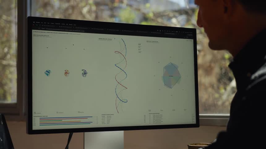 A male researcher thoughtfully examines animated DNA structures and scientific charts on a computer screen