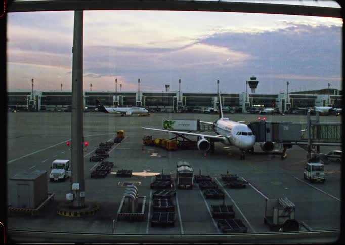 A grainy, vintage-style shot of airplanes on the airport tarmac from a terminal window at dusk