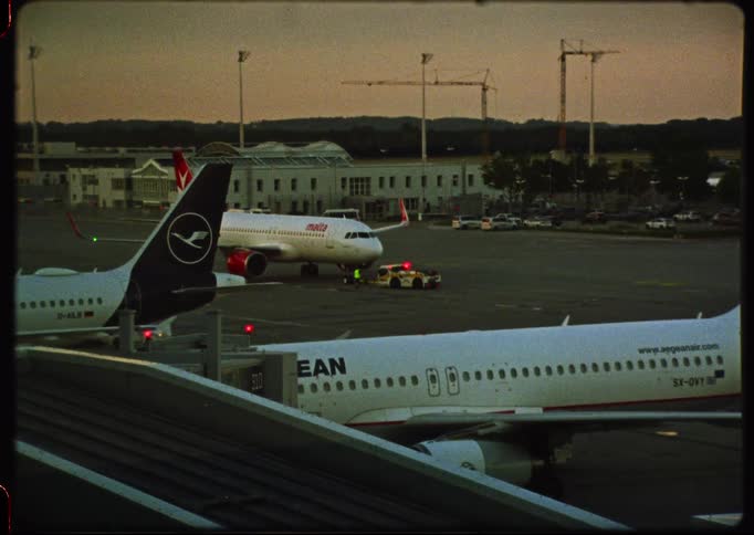 A retro-style film captures commercial airplanes parked on the airport tarmac at dusk