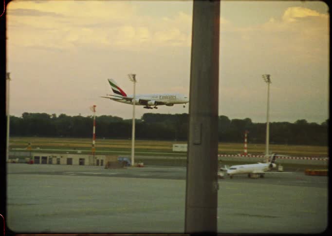 16mm analog footage shows a large Emirates passenger airplane landing on the runway at dusk