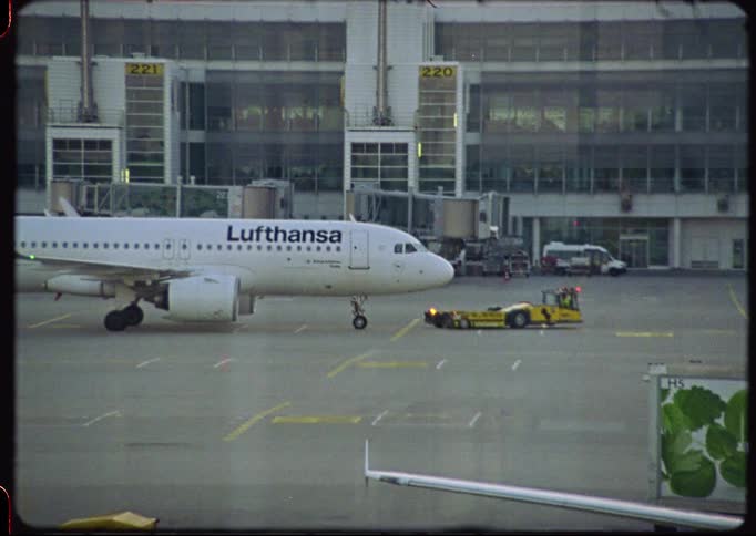 Vintage Super 8 film captures a Lufthansa airplane parked on the tarmac at an airport terminal