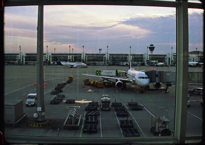16mm film captures a view from an airport window of airplanes on the tarmac at dusk