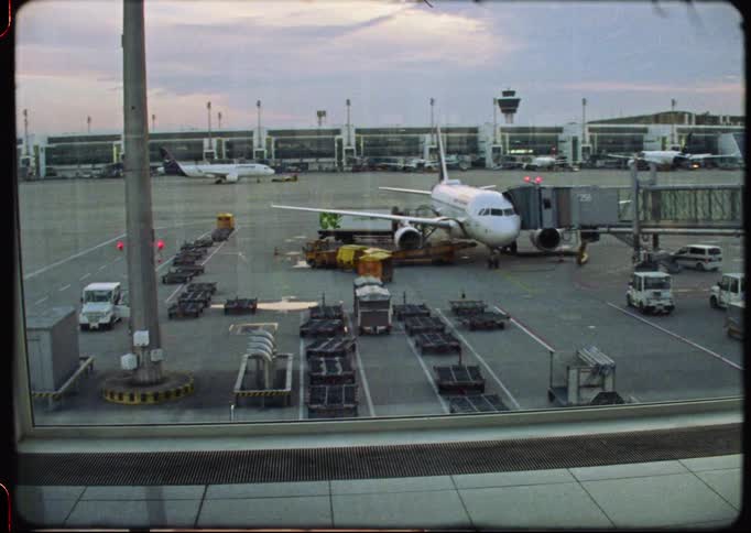 A nostalgic view from an airport terminal window shows a plane docked at the jet bridge on the tarmac, captured on grainy vintage 8mm film