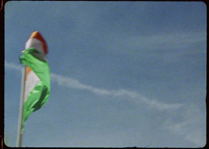 A vintage film captures a lineup of international flags from various nations waving in the breeze against a clear blue sky
