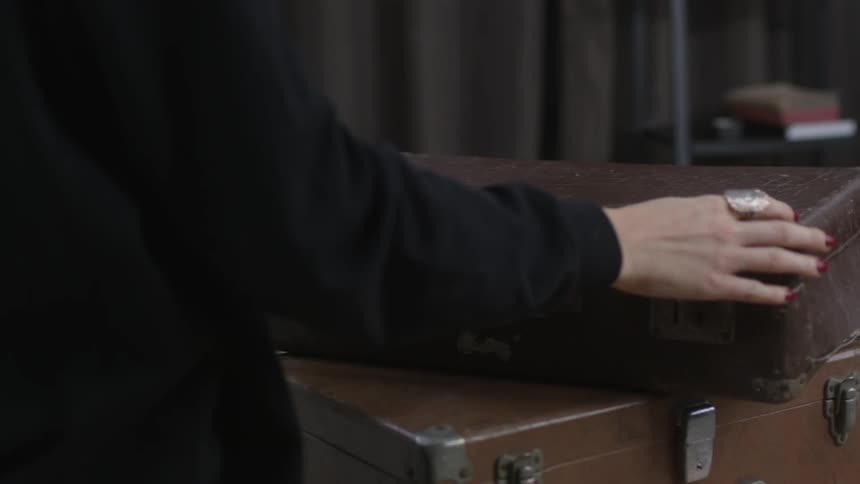 A woman closes a suitcase with clothes inside