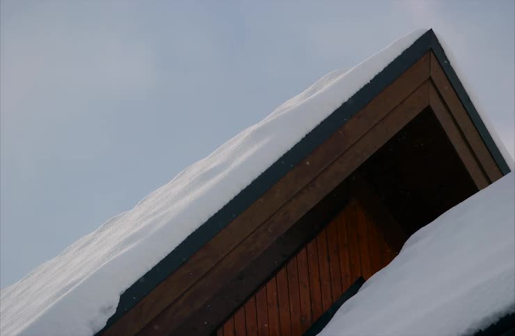 Low-angle shot of gentle snowfall on the snow-covered roof of a modern wooden house on an overcast winter day