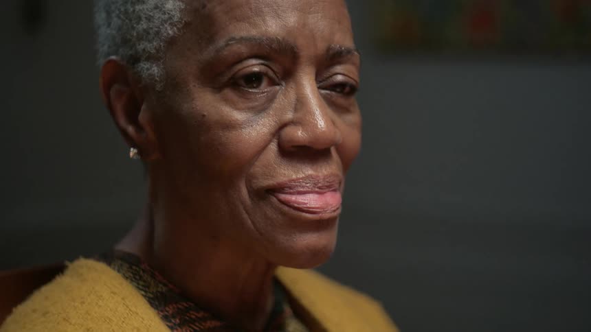 A pensive elderly African American woman slowly smiles as she reflects on a pleasant memory