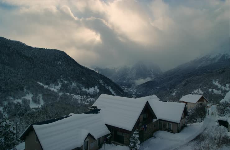 A serene view of snow-covered chalets nestled in a majestic alpine valley under a cloudy winter sky