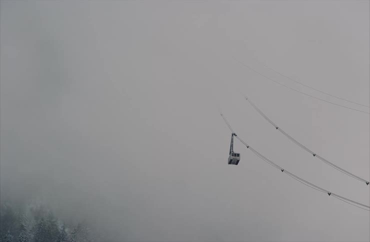 A lone cable car slowly travels through the thick gray fog above a snowy mountain forest