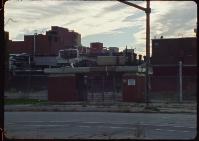 Vintage film footage captures a static shot of a desolate industrial complex from across an empty street