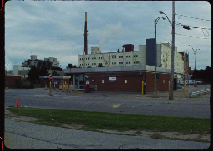 A static wide shot of a quiet industrial complex with a smokestack emitting smoke under an overcast sky