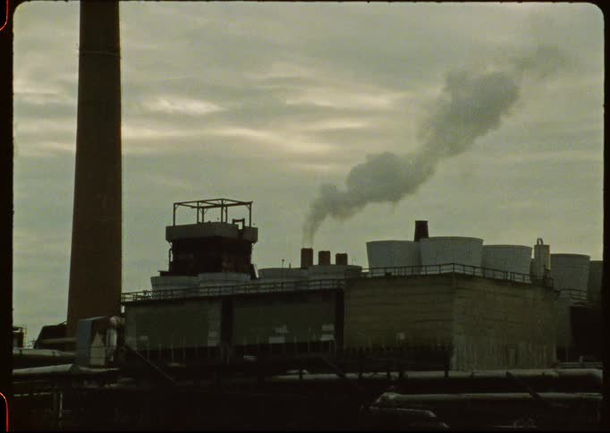 Vintage footage shows smoke billowing from a factory smokestack against an overcast sky