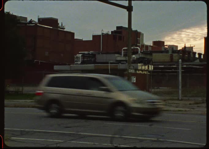 Cars drive past an abandoned building in a desolate industrial area in this vintage film shot