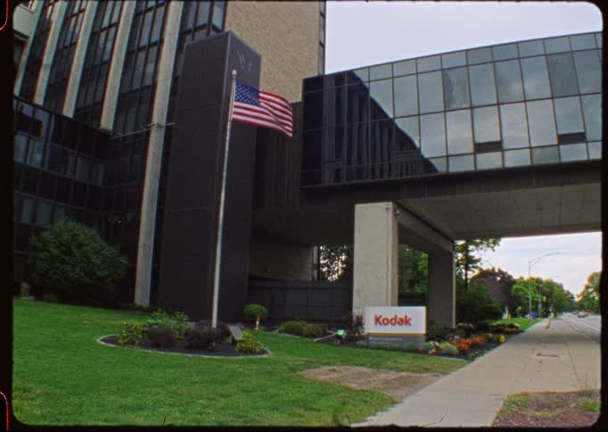 Super 8 style footage shows the Kodak logo and an American flag outside a corporate office building