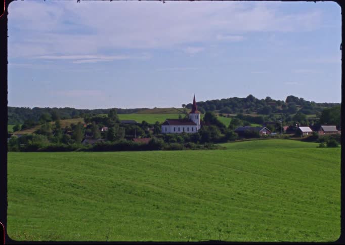Vintage Super 8 footage shows a picturesque rural village with a white church nestled in rolling green hills
