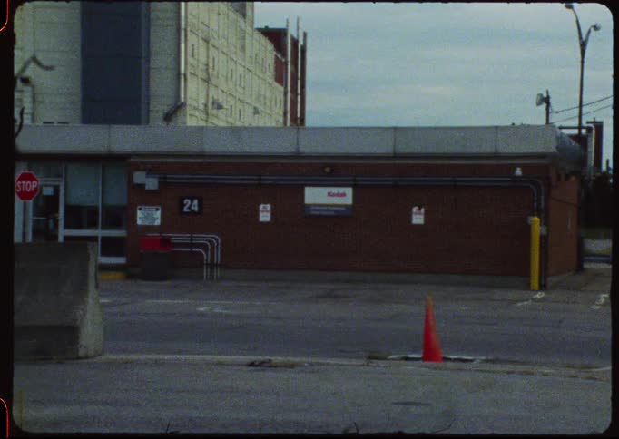 Super 8mm film captures a static shot of a desolate Kodak factory entrance on an overcast day