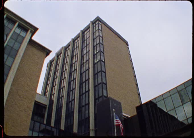 Archival-style fisheye footage tilts down a multi-story brick and glass building to reveal the Kodak company sign and an American flag