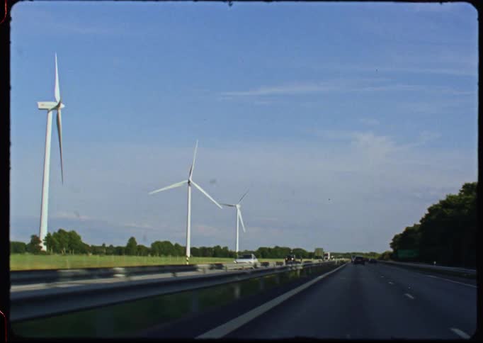 Vintage Super 8mm footage captures the view of a large wind farm from a moving car driving on the highway