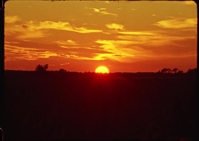 Vintage 8mm footage captures a brilliant golden sun setting over a silhouetted plain with a fiery orange sky