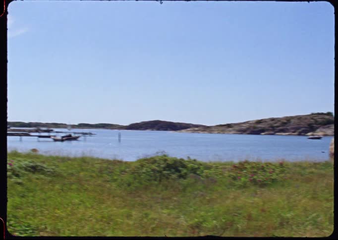 Nostalgic vintage footage captures an idyllic summer day with people swimming and relaxing by a red cabin on the rocky Swedish coast