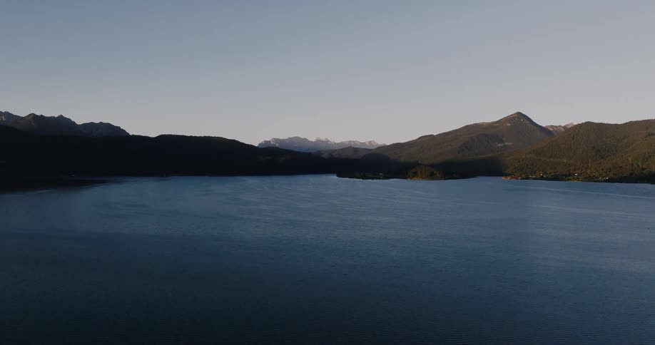 A serene aerial flight over a vast mountain lake as the golden morning sun rises over the distant peaks