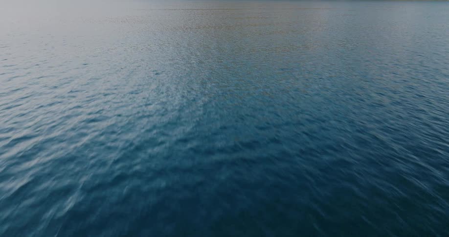 An aerial view glides low and fast over the serene, rippling surface of deep blue water