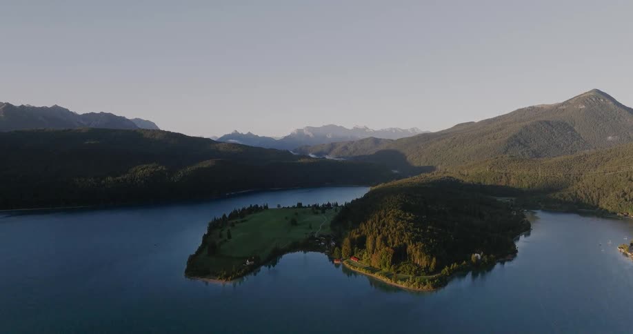 A serene aerial view of a lake and a peninsula surrounded by forested mountains at sunrise