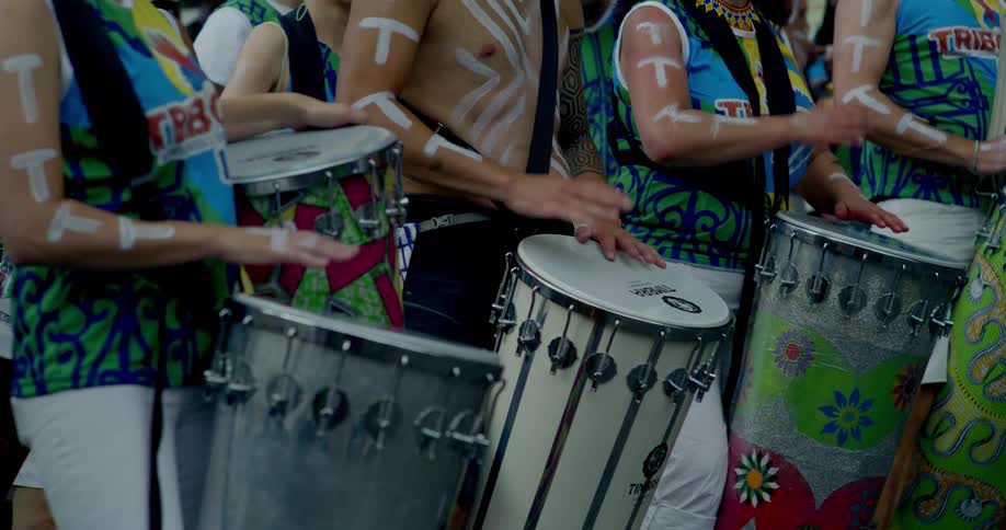 A vibrant street band with colorful costumes and body paint play their drums in unison during a festive parade