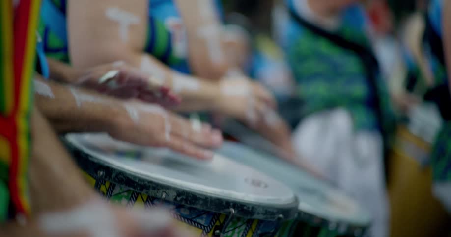 A close-up slow-motion shot of a vibrant drumming band playing hand drums in unison during a street festival