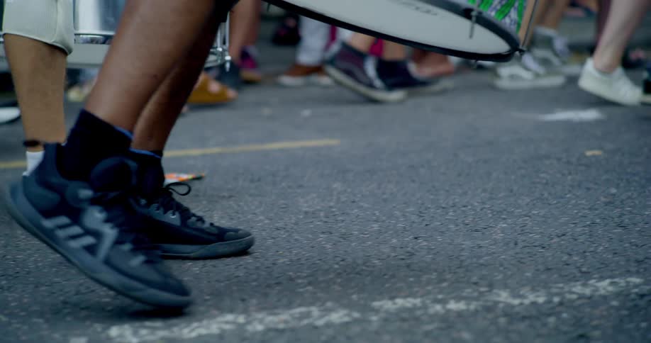 Close-up slow motion shot of the legs and feet of a marching band with colorful drums parading down a street