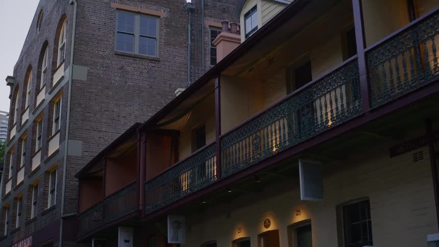 A slow zoom out on historic brick buildings with ornate balconies lining a quiet laneway at dusk