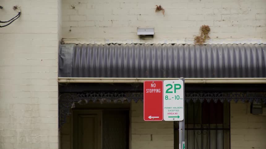 A static medium shot of Australian street parking signs in front of a grungy brick building