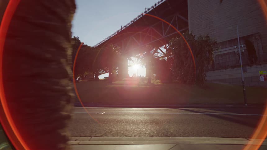Cinematic tracking shot from a low angle capturing the sun flaring from underneath the Sydney Harbour Bridge