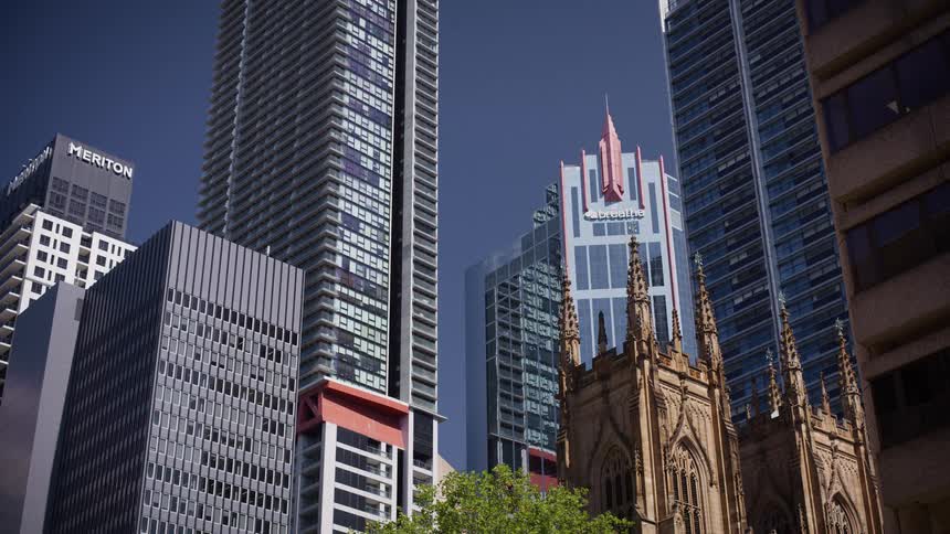 A historic gothic church stands in stark contrast to the modern skyscrapers of downtown Melbourne on a sunny day