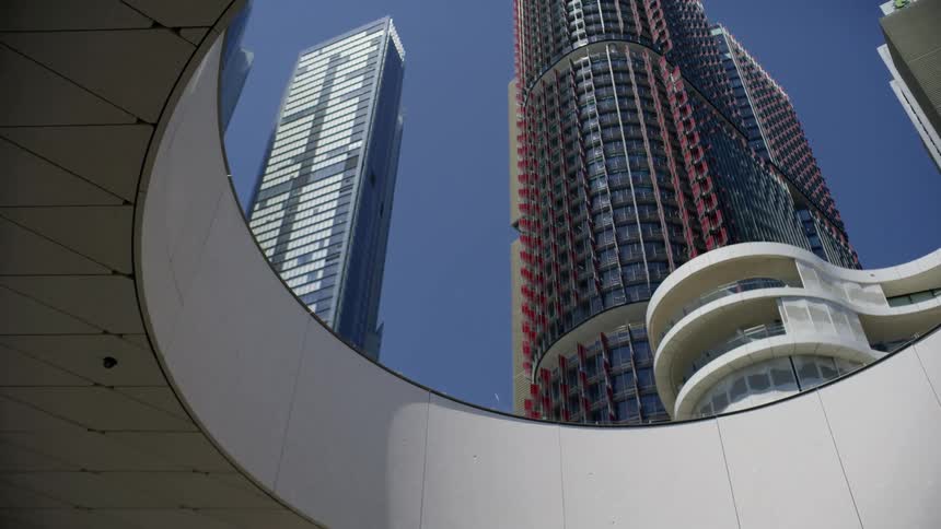 Low-angle shot revealing modern city skyscrapers through a futuristic circular architectural frame against a clear blue sky