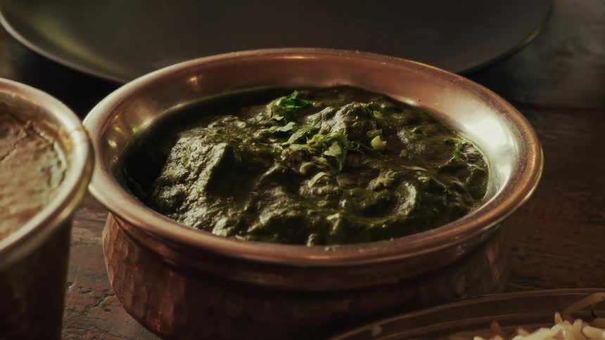 A close-up shot of a traditional Indian spinach curry, Palak Paneer, served in a rustic hammered copper bowl