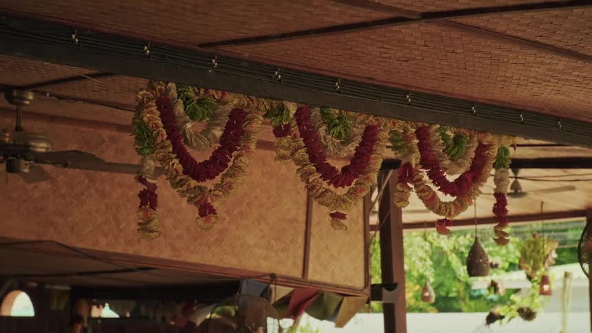 Colorful traditional Thai flower garlands gently sway from a woven bamboo ceiling in a tranquil tropical setting
